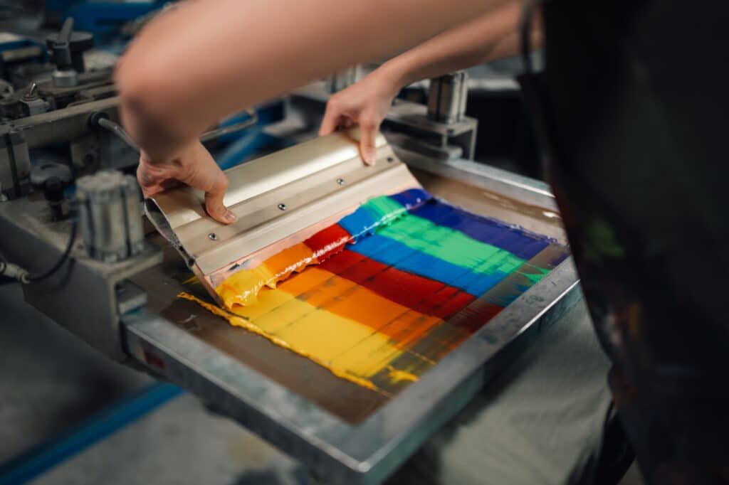 Close up of graphic worker's hands using squeegee for screen printing.